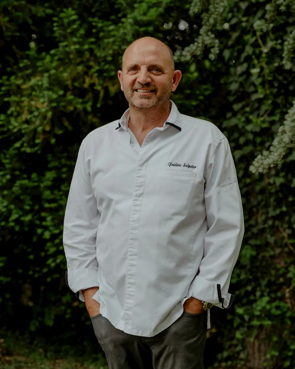 Frédéric Salpetier, chef étoilé invité, en veste de cuisine devant un mur de verdure.